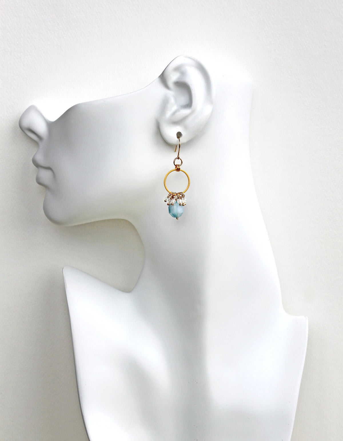 Aquamarine and gold earring on a mannequin ear with a plain background