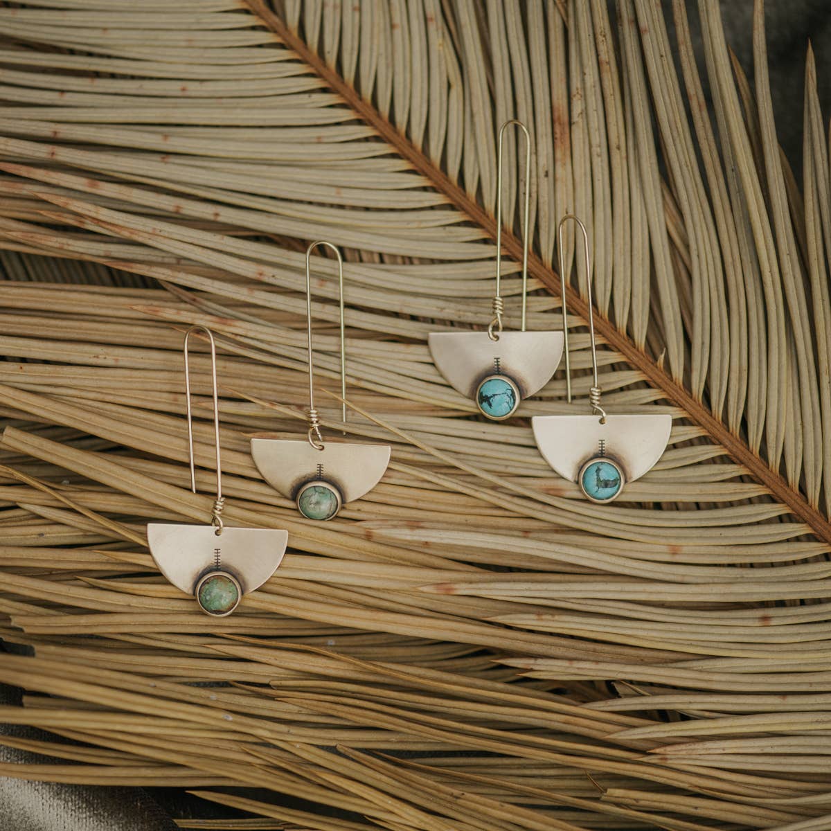 Two pair of half-moon shaped earrings with turquoise stones on a leaf background