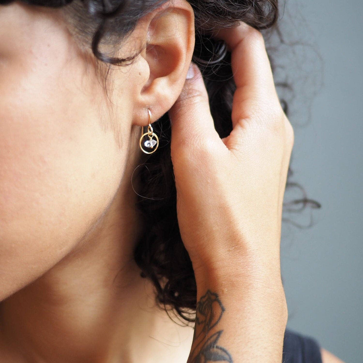 Close-up of a person wearing a gold and herkimer diamond earring with a blurred background