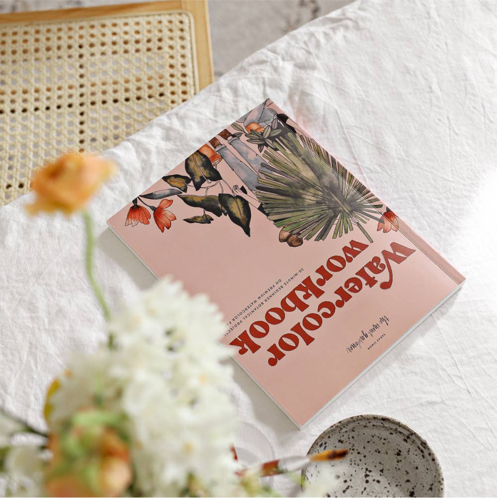 Floral watercolor book on a textured surface with flowers and a woven object in the background