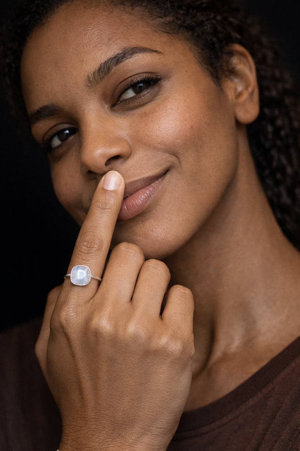 Woman with a moonstone ring on her finger against a dark background