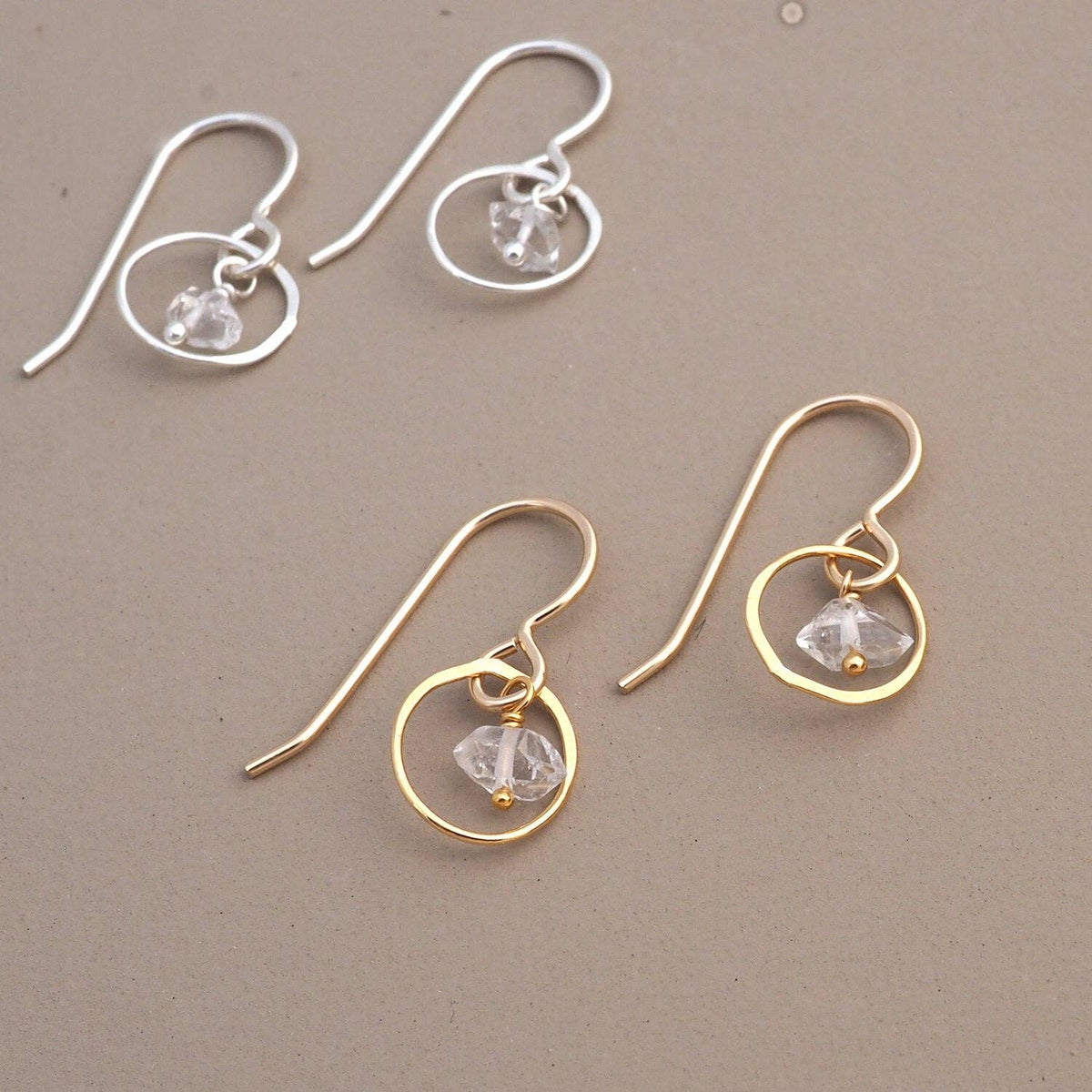 Two pairs of earrings, one gold and one silver, with circular designs and small herkimer diamonds a beige background