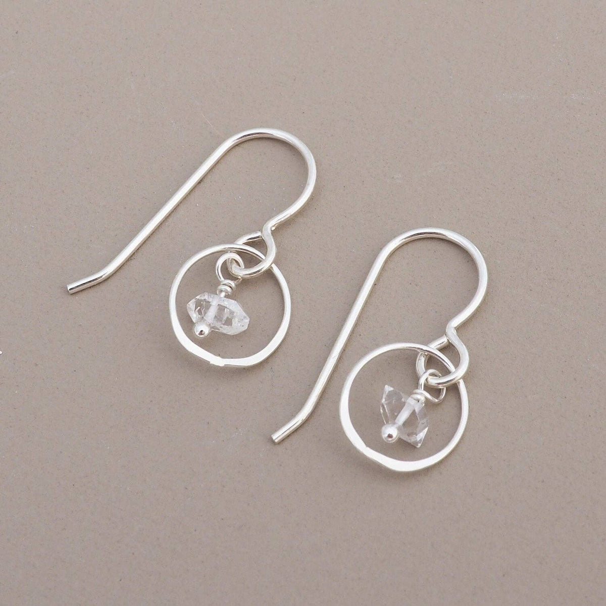 Silver earrings with circular designs and small herkimer diamonds a beige background