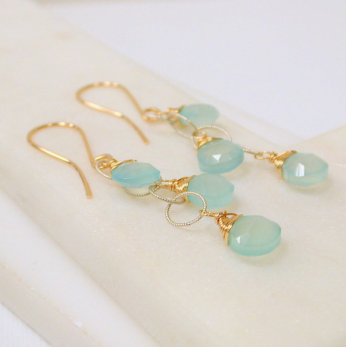Gold dangle earrings with green chalcedony beads on a white background