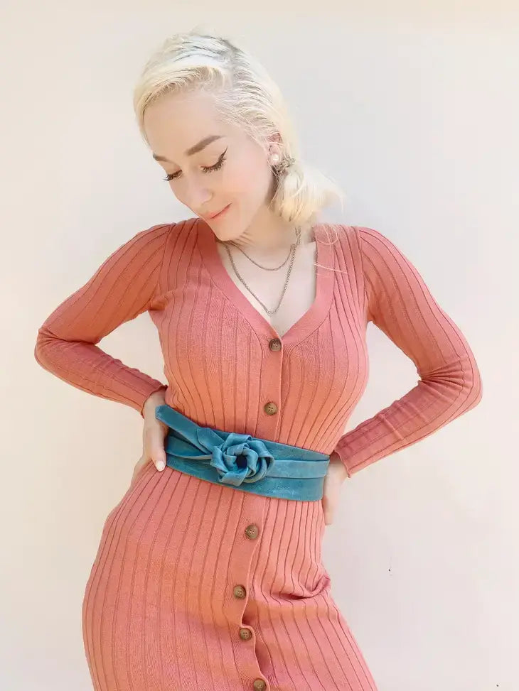 Woman wearing a pink ribbed dress with a blue belt against a white background