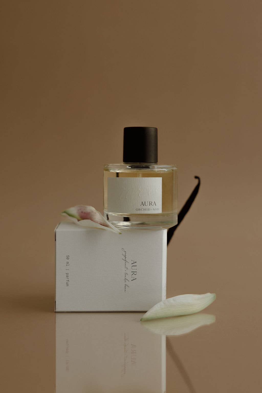 Perfume bottle labeled 'Aura' with packaging on a reflective surface and brown background