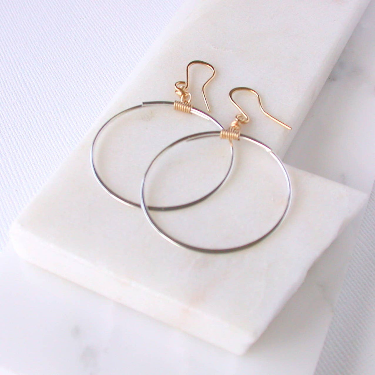 Silver hoop earrings with gold accents on a white marble surface