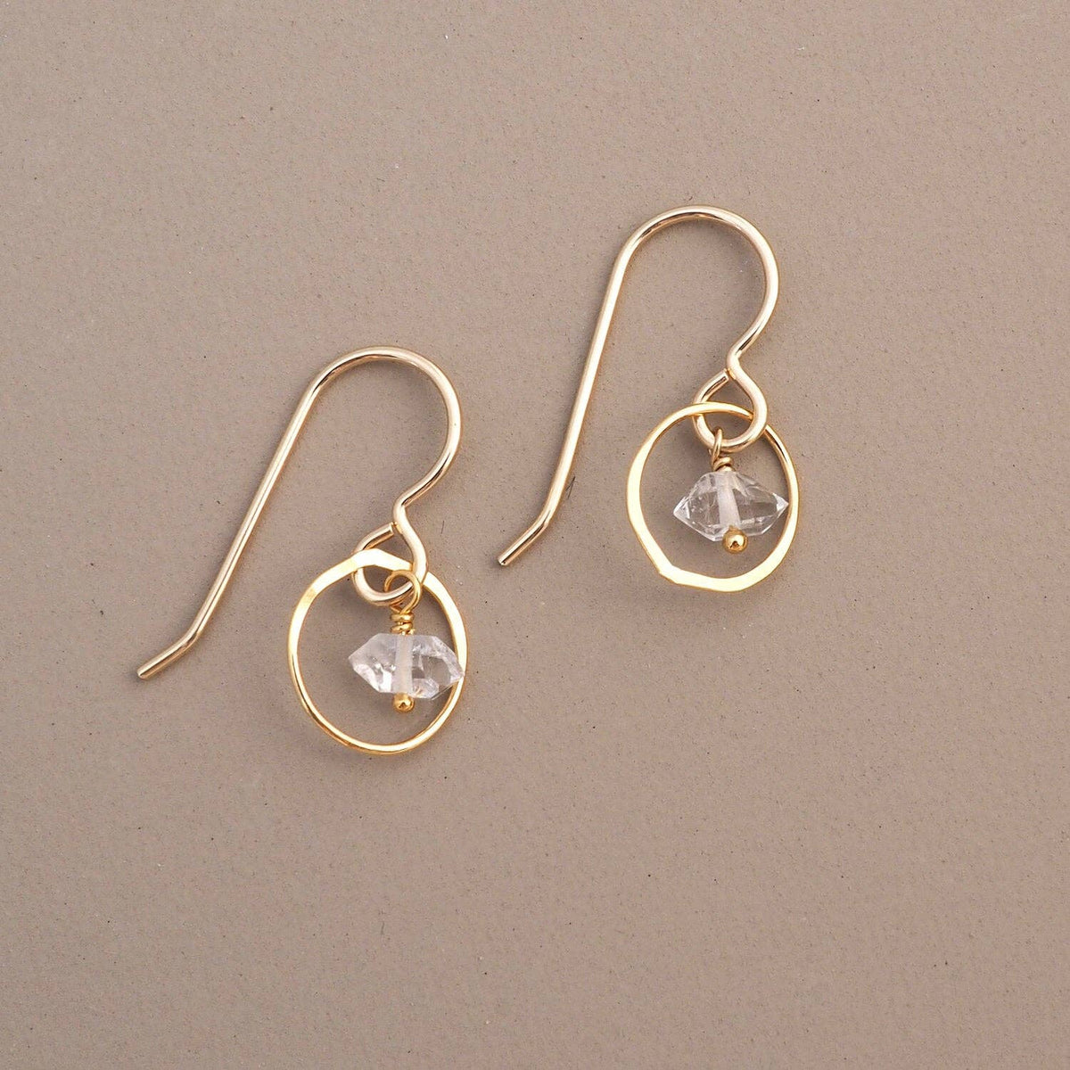 Gold earrings with circular designs and small herkimer diamonds a beige background