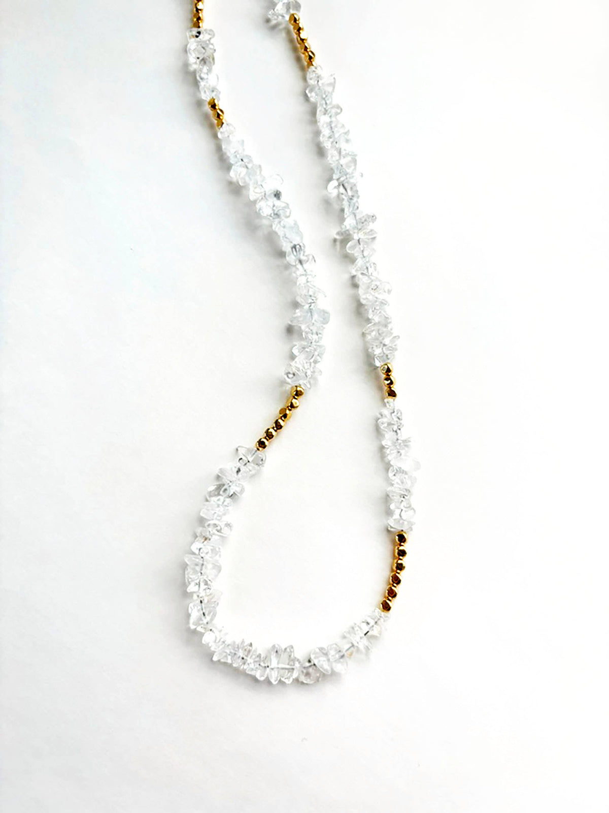 Handmade necklace with clear quartz beads and gold accents on a marble surface
