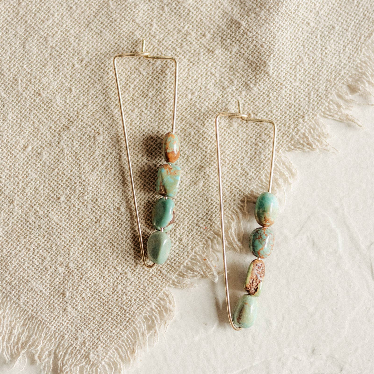 Pair of modern earrings with turquoise stones on a textured fabric background
