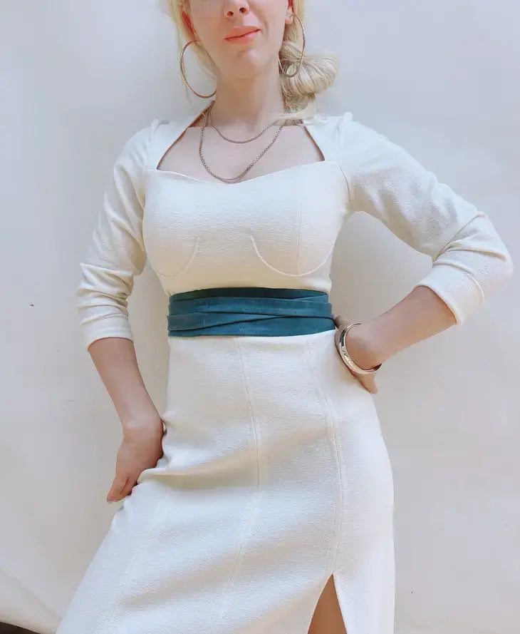 Person wearing a white outfit with a blue belt against a plain background