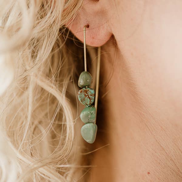 Close-up of an ear wearing a turquoise stone earring with blonde hair.