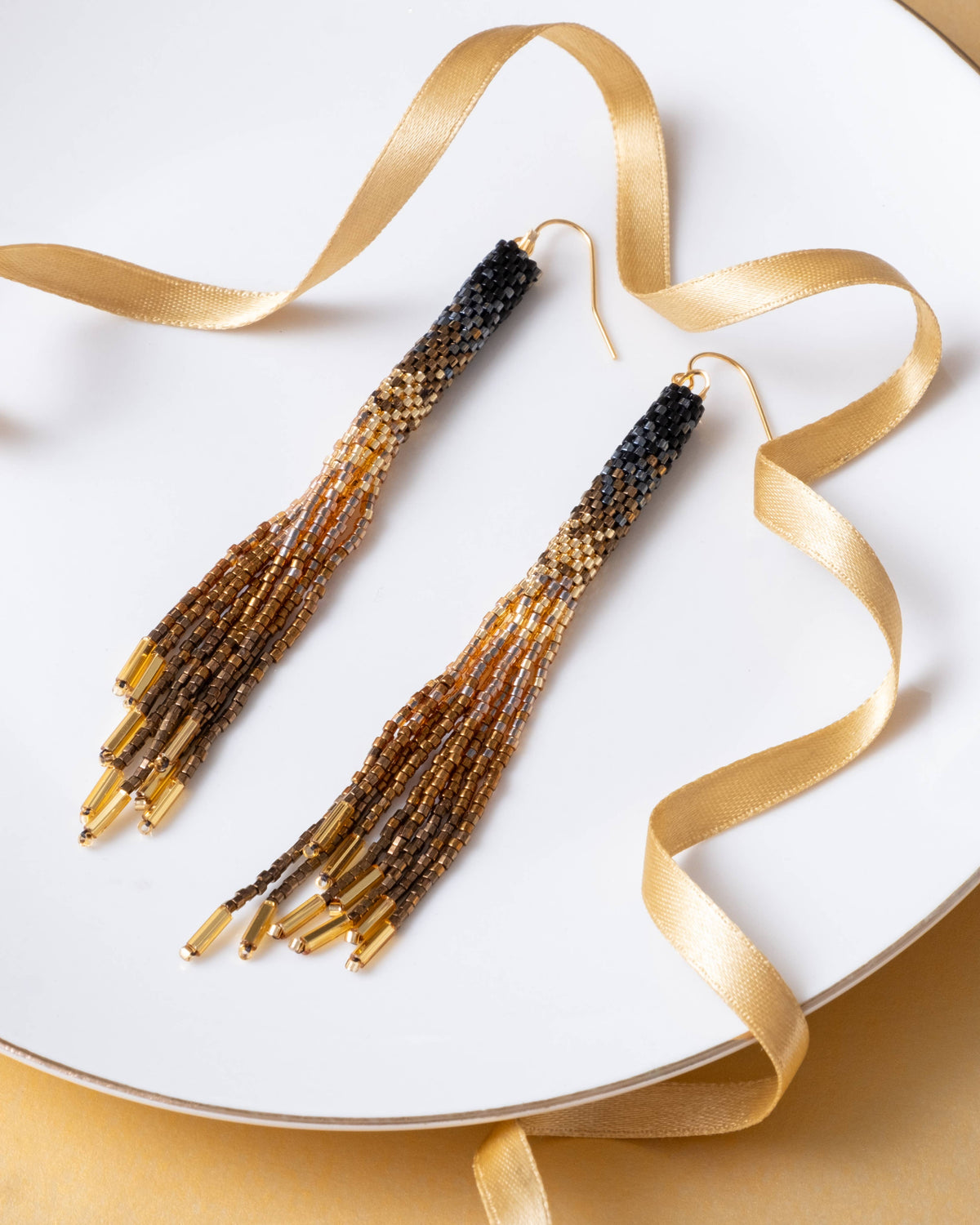 Pair of beaded tassel earrings on a white plate with gold ribbon
