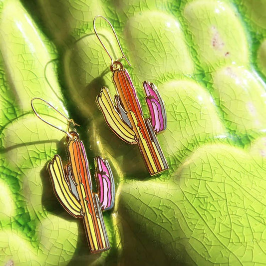 Colorful cactus-shaped earrings on a green leaf background