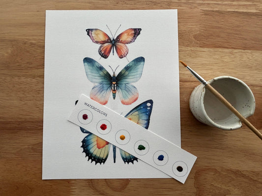 Butterfly illustration on paper with watercolor swatches and a paintbrush on a wooden surface