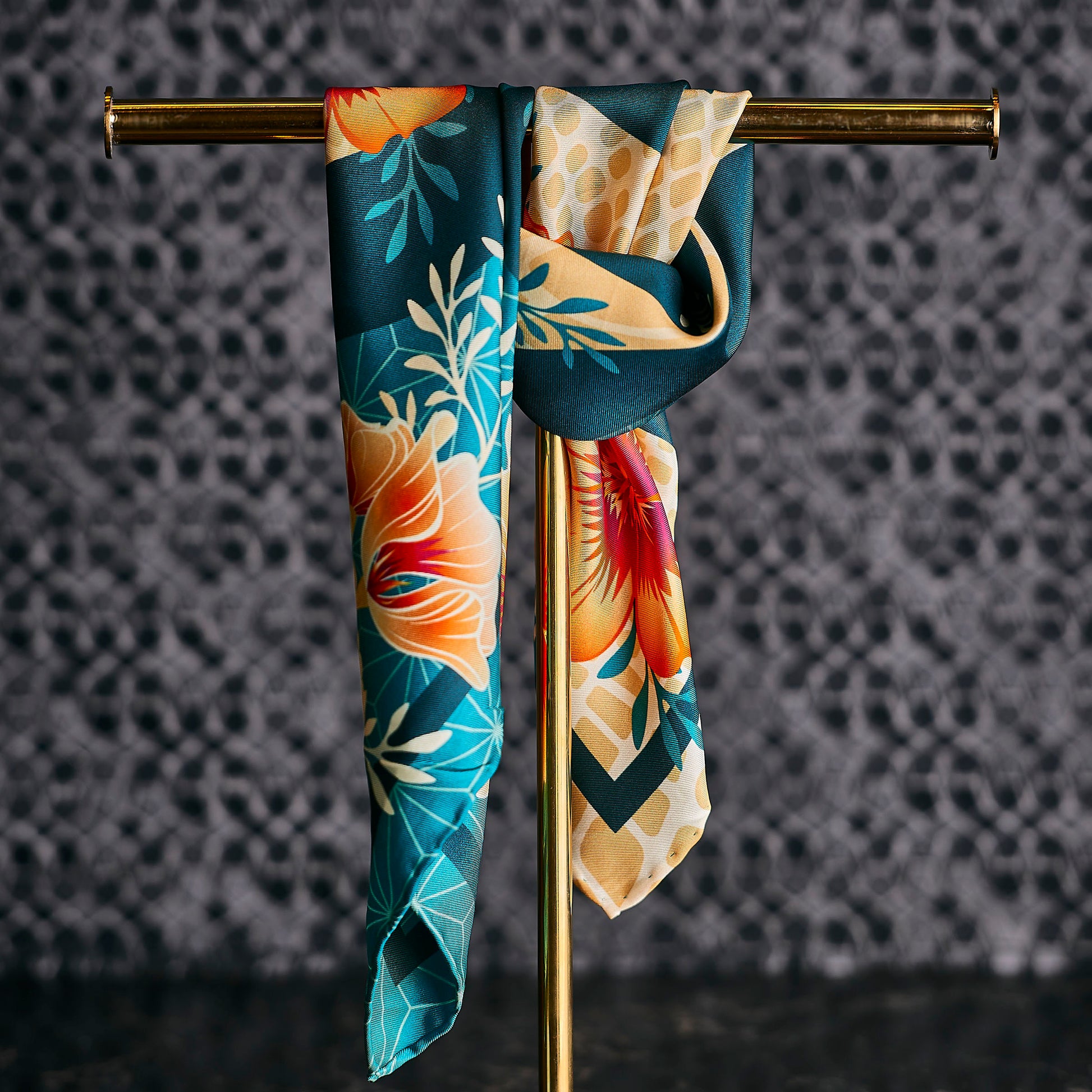 Blue and Orange Floral scarf hanging on a gold rod against a textured gray background