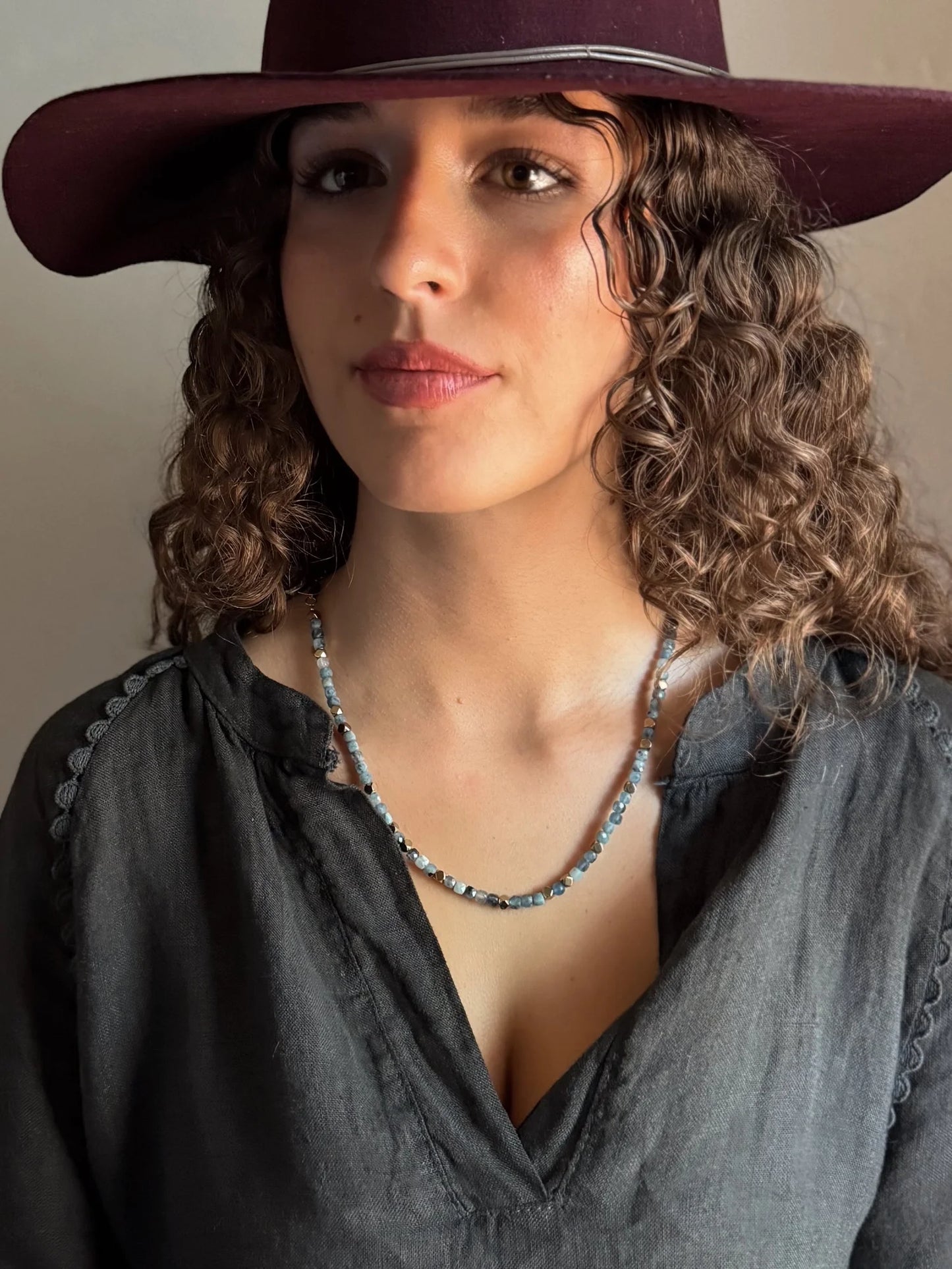 Woman wearing a wide-brimmed hat and dark blouse with a beaded necklace.