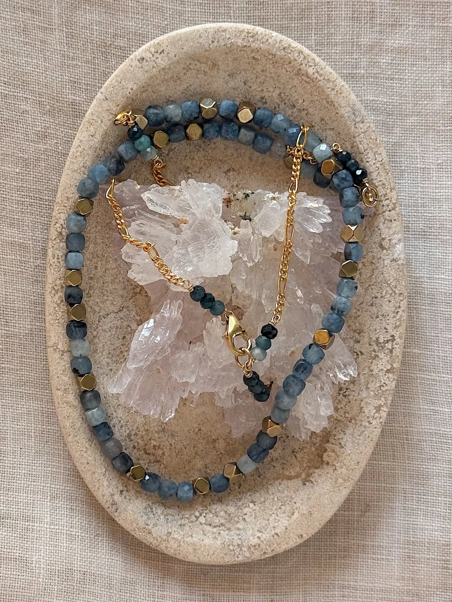 Necklace with blue beads and gold accents on a stone surface with crystal rock