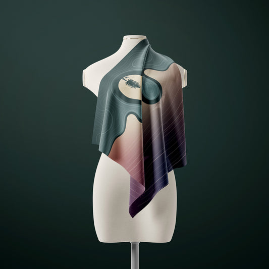 A draped silk scarf with an abstract landscape design in shades of teal, pink, and purple, displayed on a cream-colored mannequin torso against a dark green background.