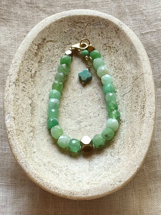 Green aventurine beaded bracelet with gold clasp on a textured stone surface