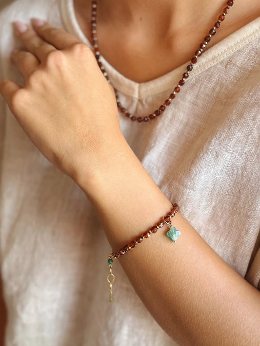 Close-up of a person's arm wearing a garnet bracelet with a heart charm on a neutral background