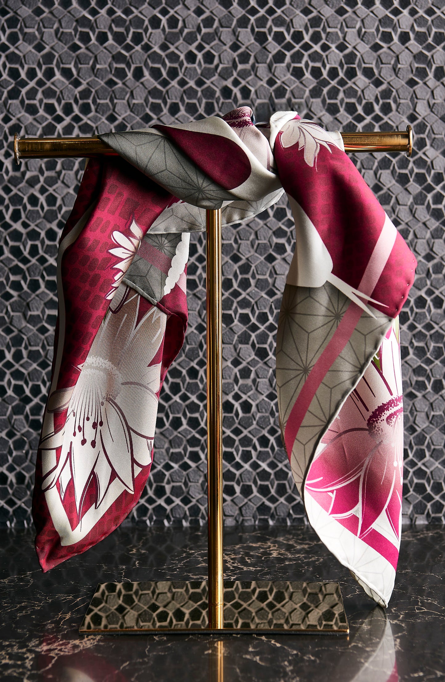 Decorative scarf with floral pattern draped over a gold stand against a textured wall.