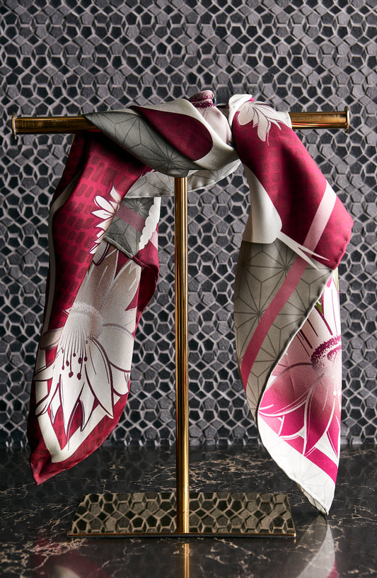 Decorative scarf with floral pattern draped over a gold stand against a textured wall.
